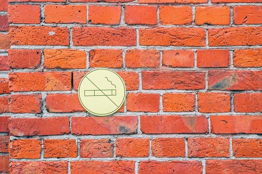 No smoking sign on a red brick wall, indicating a smoke-free zone. The simple design contrasts with the textured bricks.