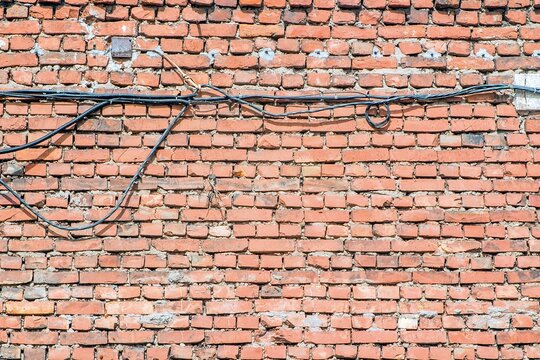 Rugged red brick wall with visible mortar and tangled black cables running horizontally across it, displaying an urban and industrial aesthetic