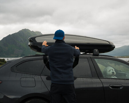 Man closes car roof box in scenic mountain landscape