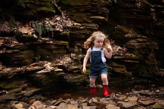 Young girl in red boots explores a rocky creek