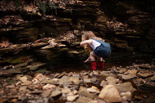 Little girl in red boots plays in a rocky stream