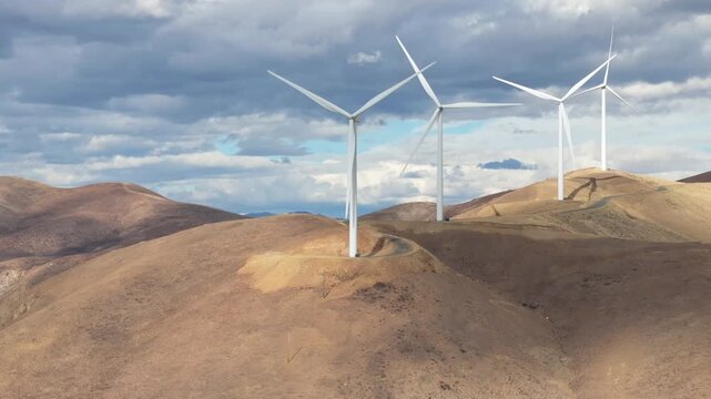 Wind turbines rise on arid hills under changing sky
