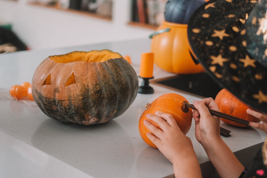 A close-up shot of the hands of children and their mother carving Halloween pumpkins on the kitchen table. Preparing and decorating the home for the main autumn holiday for children. Trick or treat.