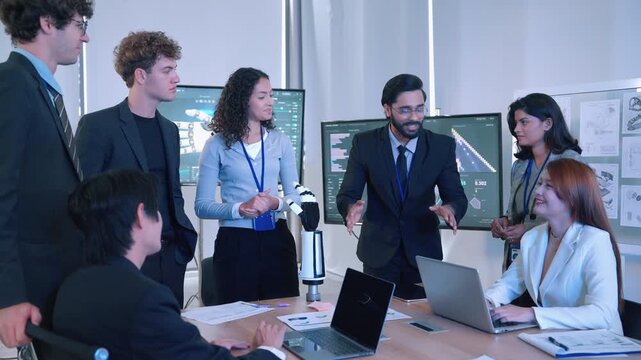 Diverse engineering team discussing a robotic hand prototype while reviewing digital engineering data and technical drawings in a modern workplace.
