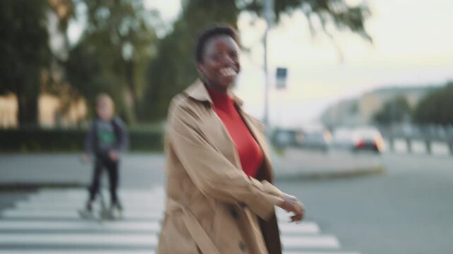 Follow view of black woman walking on pedestrian crossing in downtown, back view . Young adult african american lady strolling alone in city in warm weather in autumn season, smiling to camera