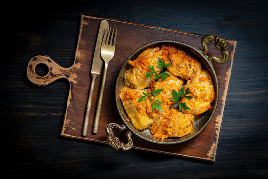 Traditional stuffed cabbage rolls in rustic pan, closeup. Top view of savory homemade cabbage rolls with tomato sauce and parsley served in vintage metal pan on dark wooden background
