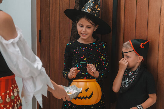 A medium shot of children in Halloween costumes opening doors and holding out pumpkin shaped baskets while saying Trick or treat. Celebrating Halloween with children and collecting candy.