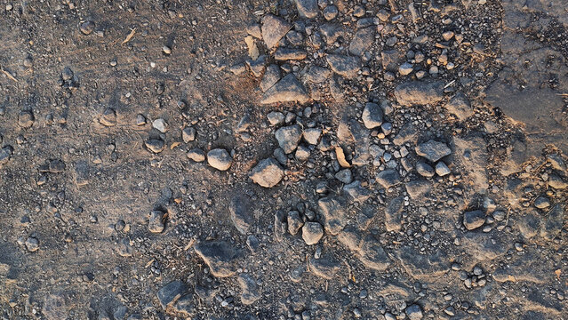 Rough Weathered Asphalt Road Surface with Exposed Stone Aggregate. Close-up of a rough weathered asphalt road surface with exposed stone aggregate, gravel particles, and an uneven dark gray pavement