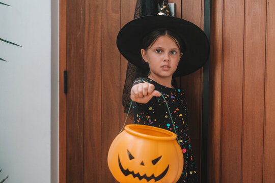 A portrait of a girl in a witch costume, out trick or treating with a pumpkin shaped basket. Trick or treat. An autumn children's celebration during the spooky season.
