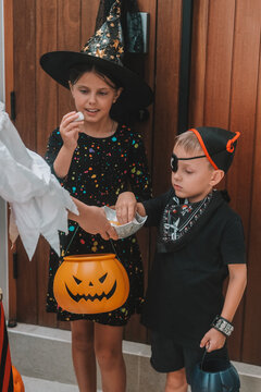A medium shot of children in Halloween costumes opening doors and holding out pumpkin shaped baskets while saying Trick or treat. Celebrating Halloween with children and collecting candy.