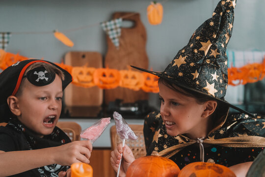 A medium shot of children in Halloween costumes decorating their home, carving a pumpkin, and eating gummy candies. They are playing together and celebrating Halloween in the kitchen. Trick or treat.