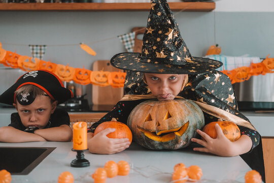 A medium shot of children in Halloween costumes decorating their home, carving a pumpkin, and eating gummy candies. They are playing together and celebrating Halloween in the kitchen. Trick or treat.