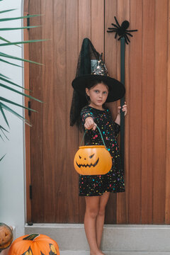 A portrait of a girl in a witch costume, out trick or treating with a pumpkin shaped basket. Trick or treat. An autumn children's celebration during the spooky season.