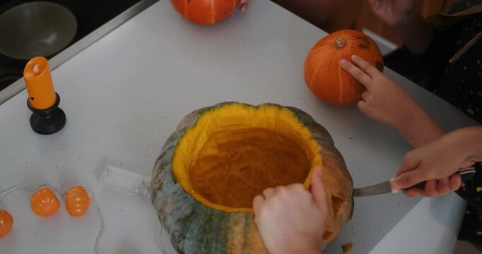 A close-up shot of the hands of children and their mother carving Halloween pumpkins on the kitchen table. Preparing and decorating the home for the main autumn holiday for children. Trick or treat.