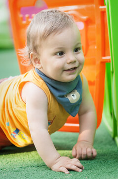 A cheerful baby crawls on a vibrant green surface, surrounded by bright orange and green play structures. The sunlight bathes the scene, highlighting the joy of childhood exploration.