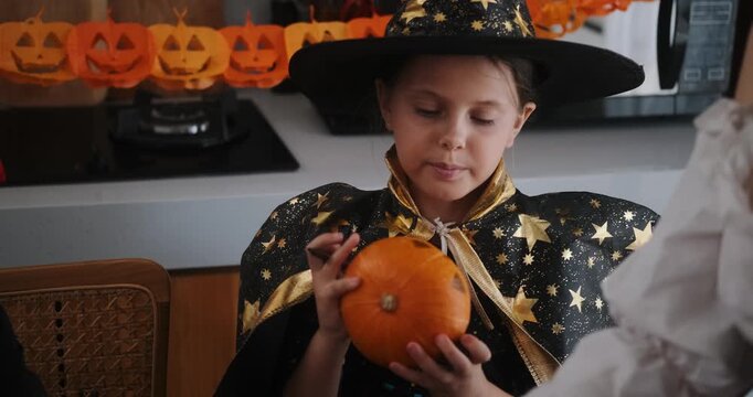 A close-up shot of the hands of children and their mother carving Halloween pumpkins on the kitchen table. Preparing and decorating the home for the main autumn holiday for children. Trick or treat.