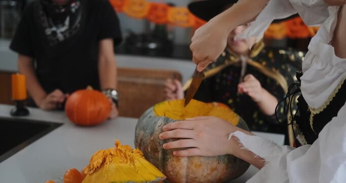 A close-up shot of the hands of children and their mother carving Halloween pumpkins on the kitchen table. Preparing and decorating the home for the main autumn holiday for children. Trick or treat.