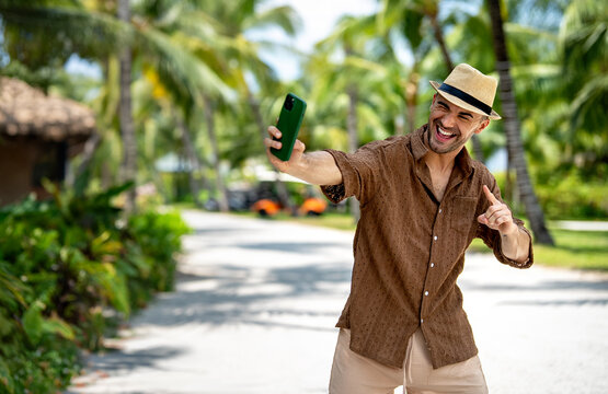 Happy tourist young man enjoying a sunny day and taking photos in a tropical resort on vacation