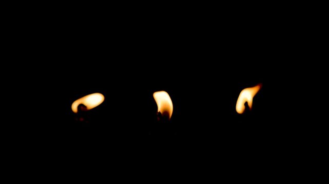 Breeze blowing out candle flame dark view closeup. Wax taper fire ending on black background. Night glowing dimly with flickering light. Smoke curling up slowly from wick. Peaceful atmosphere concept