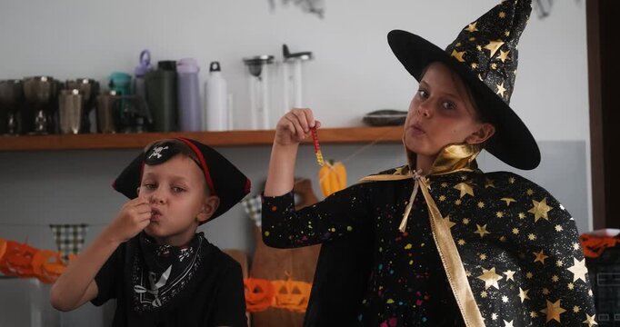 A medium shot of children in Halloween costumes decorating their home, carving a pumpkin, and eating gummy candies. They are playing together and celebrating Halloween in the kitchen. Trick or treat.