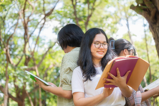 Cheerful college girls holding textbooks and studying on university campus, Group of asian female students reading books together outdoors at park, Young friends reading and learning in green garden