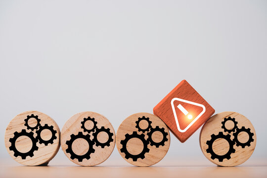 Business process risk and operational disruption concept with a warning symbol interrupting wooden gear blocks for workflow problems and system failure management.