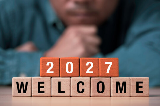 Welcome 2027 New Year concept with wooden letter and number blocks in front of a thoughtful person symbolize business fresh beginnings and future planning opportunities.