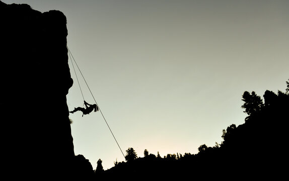 Rock climber descending a cliff face with ropes during a scenic twilight