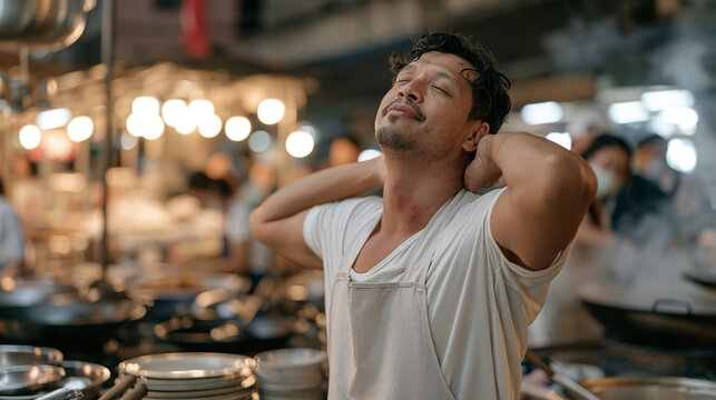 A Thai street food vendor scratching the back of his neck while fanning charcoal smoke away from his face, heat rash creeping up under his collar, busy night market behind him