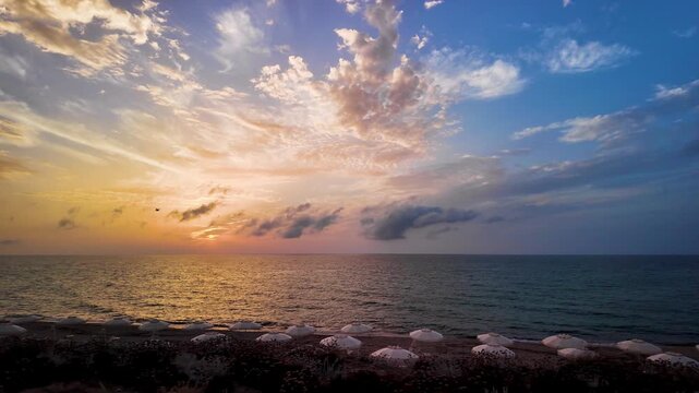 Golden sunset over the sea horizon on an empty sandy beach with umbrellas