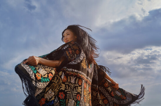 Woman dances outdoors in an embroidered patchwork robe under the sky