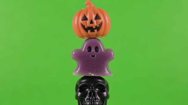 Dynamic Halloween candy stack. Orange jack-o'-lantern, purple ghost, black skull assemble on bright green screen, ideal for spooky holiday visuals.