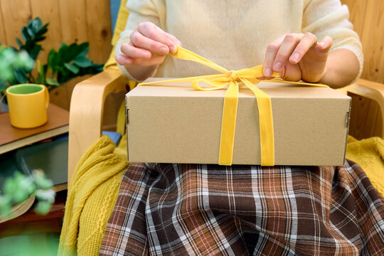 Woman sitting in armchair holding gift box with yellow ribbon