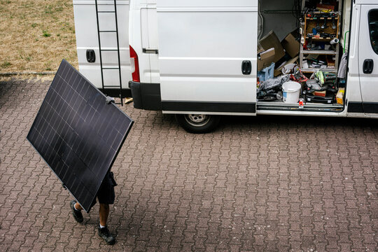 Worker carries solar panel near van during PV system installation