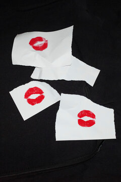 Torn white paper notes show red lipstick kiss marks on black fabric