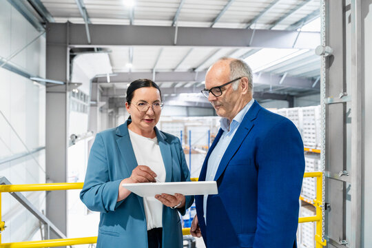 Businesswoman and businessman review tablet in warehouse