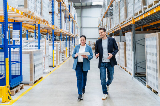 Man and woman walk through a warehouse discussing logistics