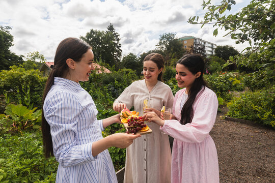 Smiling woman shares fruit board with friend in the garden