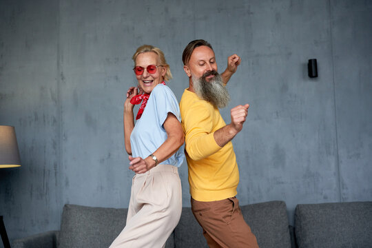 Happy senior woman and mature man dancing back to back indoors
