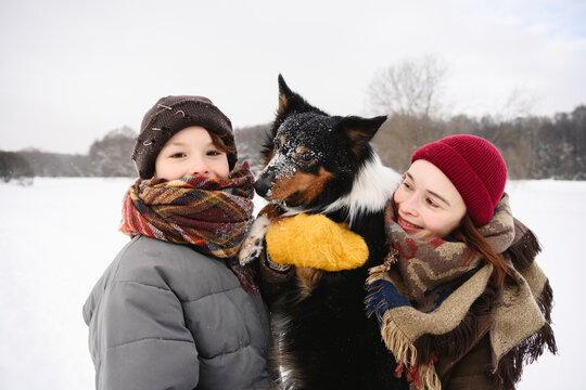 Mother and child outdoors in winter petting dog and enjoying snow