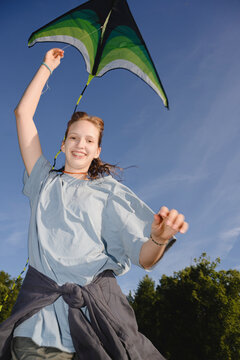 Happy girl flies a green kite outdoors under a clear blue sky