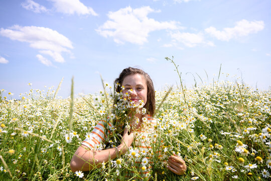 A smiling woman holds a daisy in a sunny summer meadow outdoors