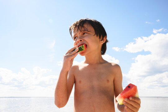 A happy boy eats a sweet watermelon at the beach during summer