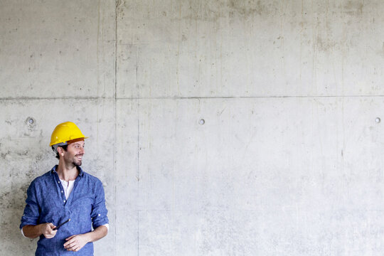 Smiling man with hard hat on construction site at concrete wall