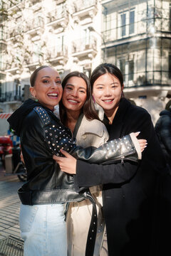 Smiling female friends are hugging each other on a city street