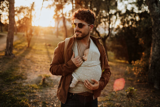 Father carries his sleeping baby in a carrier at the park
