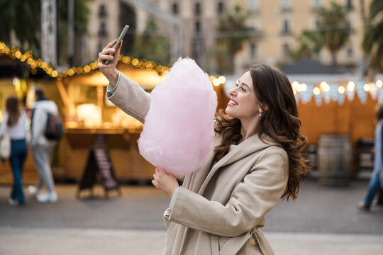 Smiling woman takes a selfie with cotton candy at an outdoor market