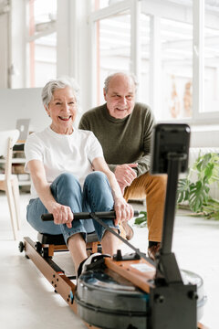 Smiling woman rows on a machine while man cheers her on indoors