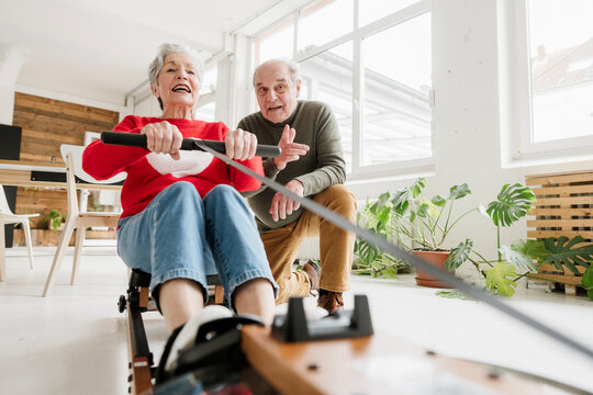 Senior woman exercising on rowing machine while senior man cheers