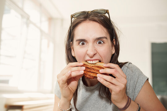 Hungry woman aggressively bites into food indoors